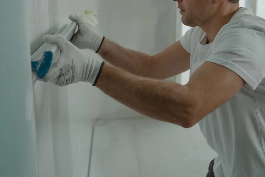 Two gloved hands smoothing joint compound onto a drywall wall with a taping knife