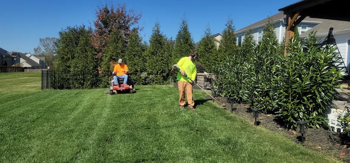 A two-man landscaping crew working a lawn — one on the mower, one on the trimmer