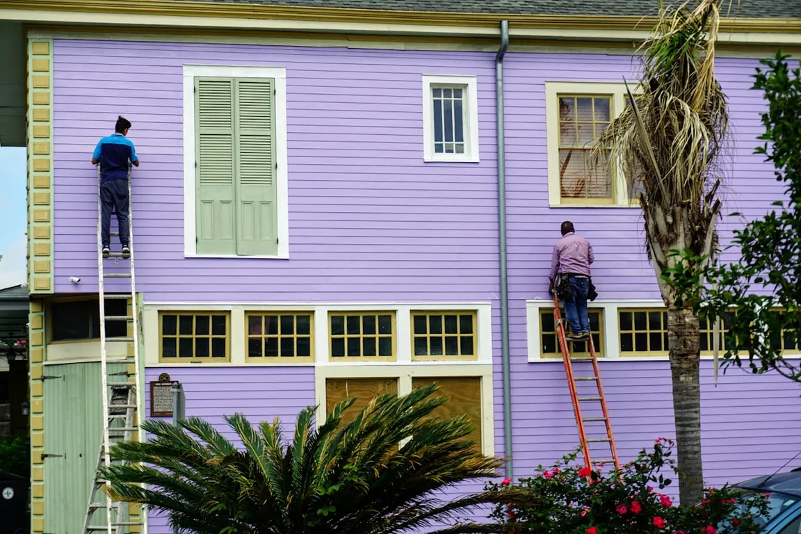 Two painters working up ladders on a home exterior