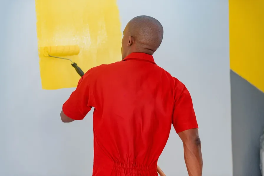 A painter rolling bright yellow paint onto a wall in clean, even strokes