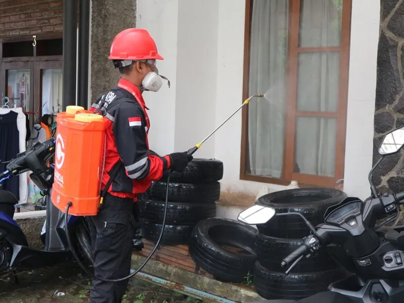 A pest control technician in protective gear treating a home exterior with a backpack sprayer