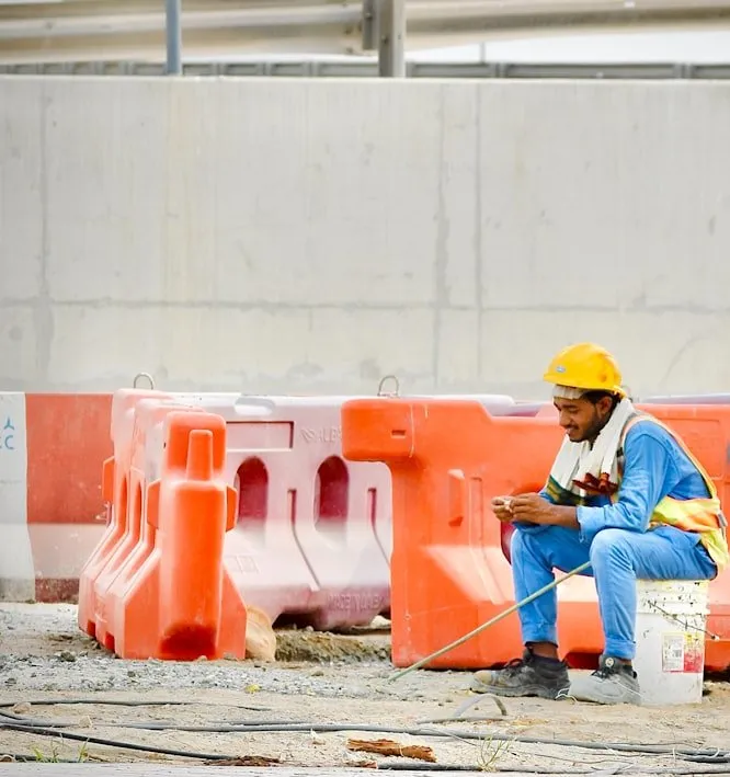 A tradesman sitting on a bucket at a quiet jobsite, checking his phone